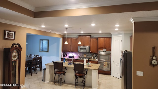 kitchen featuring a kitchen island with sink, stainless steel appliances, a kitchen breakfast bar, light stone counters, and decorative light fixtures