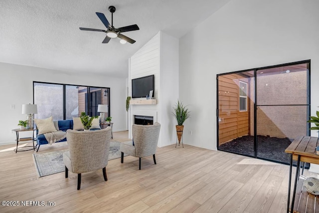 living room featuring ceiling fan, high vaulted ceiling, a textured ceiling, and light wood-type flooring