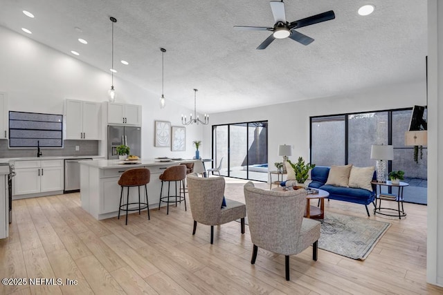 living room with sink, high vaulted ceiling, a textured ceiling, light hardwood / wood-style floors, and ceiling fan with notable chandelier