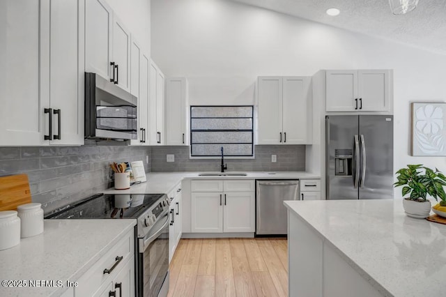 kitchen with sink, white cabinetry, stainless steel appliances, light stone counters, and vaulted ceiling