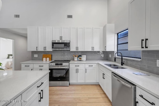 kitchen featuring sink, light hardwood / wood-style flooring, stainless steel appliances, a high ceiling, and white cabinets