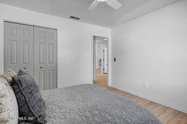 bedroom featuring ceiling fan, a textured ceiling, light hardwood / wood-style floors, and a closet