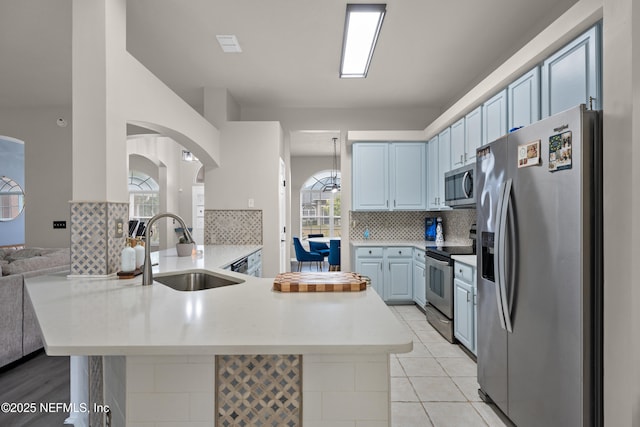 kitchen with light tile patterned flooring, sink, tasteful backsplash, kitchen peninsula, and stainless steel appliances