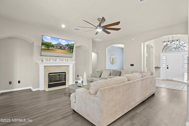 living room featuring hardwood / wood-style flooring, ceiling fan with notable chandelier, and a high end fireplace