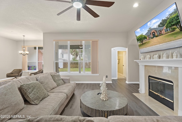 living room with wood-type flooring, ceiling fan with notable chandelier, a textured ceiling, and a fireplace