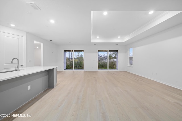 unfurnished living room with ornamental molding, a raised ceiling, sink, and light hardwood / wood-style flooring