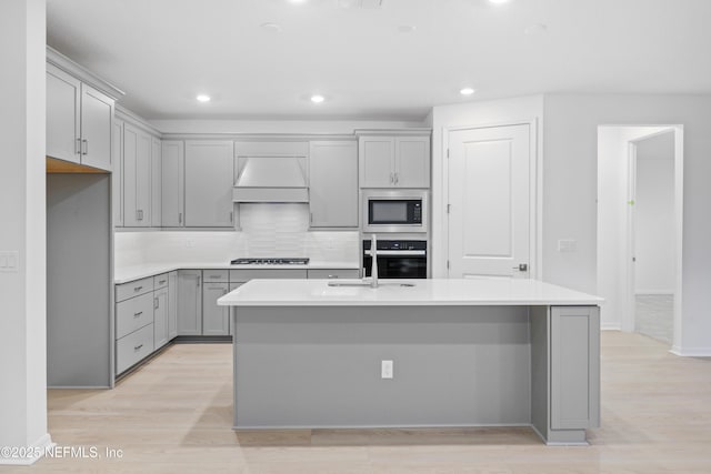 kitchen with black gas cooktop, wall oven, an island with sink, built in microwave, and custom exhaust hood