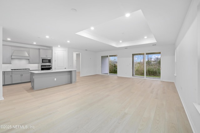 unfurnished living room with light wood-type flooring and a tray ceiling