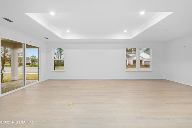 empty room with ornamental molding, light hardwood / wood-style flooring, and a tray ceiling