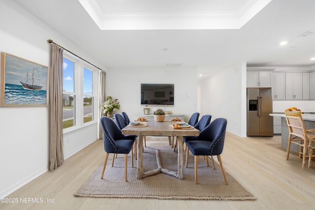 dining space featuring a tray ceiling, crown molding, and light hardwood / wood-style flooring