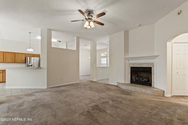 unfurnished living room featuring light carpet, ceiling fan, a fireplace, and a textured ceiling