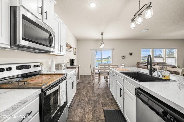 kitchen with white cabinetry, appliances with stainless steel finishes, hanging light fixtures, light stone counters, and sink