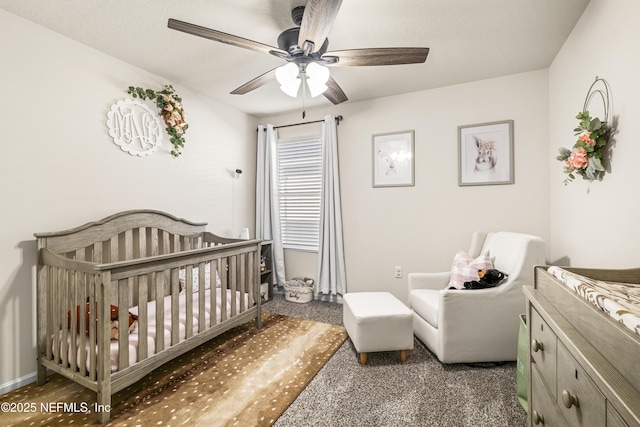 bedroom with ceiling fan, a nursery area, and dark colored carpet