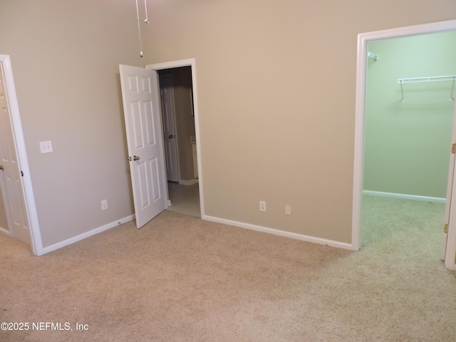 unfurnished bedroom with a walk in closet, a closet, and light colored carpet