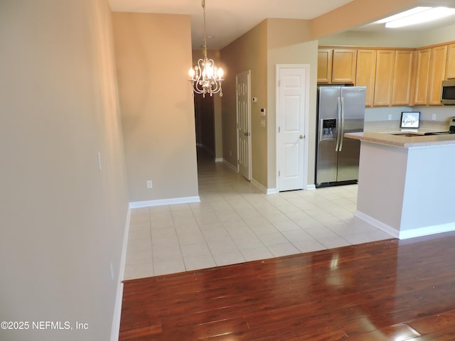 kitchen featuring appliances with stainless steel finishes, decorative light fixtures, light brown cabinetry, a chandelier, and light tile patterned flooring