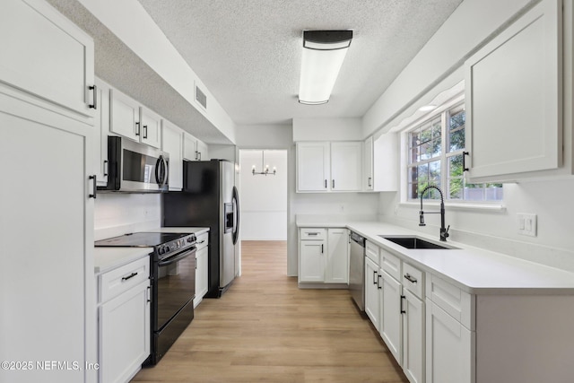 kitchen with sink, an inviting chandelier, stainless steel appliances, a textured ceiling, and white cabinets