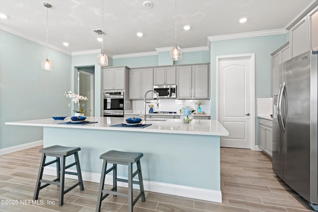 kitchen featuring a center island with sink, stainless steel appliances, a breakfast bar, gray cabinets, and pendant lighting