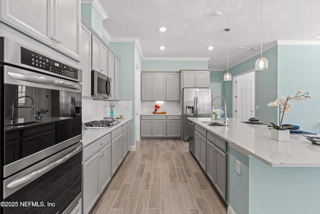 kitchen featuring an island with sink, gray cabinetry, sink, appliances with stainless steel finishes, and pendant lighting