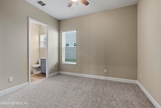 carpeted spare room with ceiling fan and connected bathroom