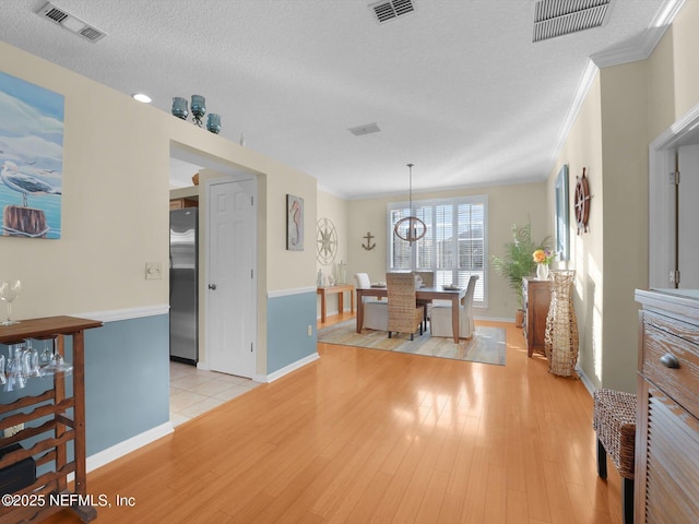 dining room with a textured ceiling, crown molding, and light hardwood / wood-style floors