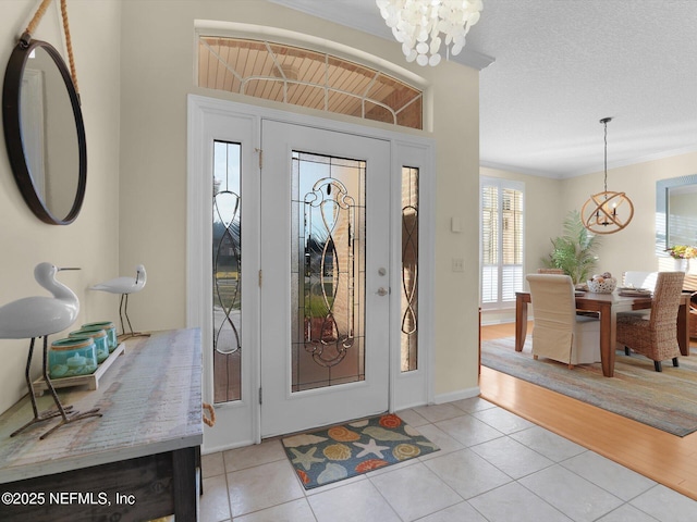 tiled entryway with a textured ceiling, a chandelier, and ornamental molding