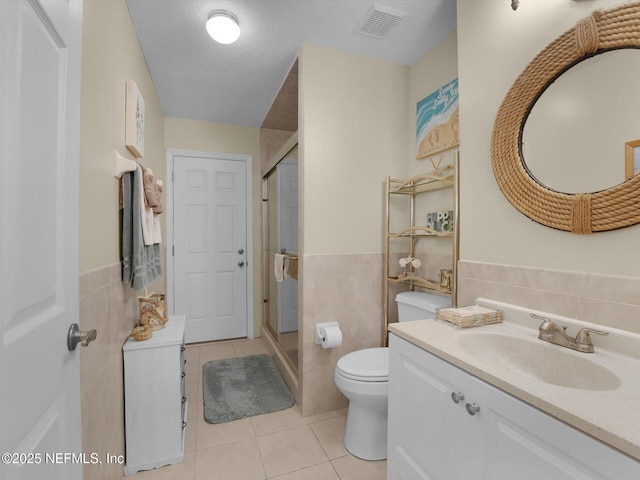 bathroom featuring a textured ceiling, tile patterned floors, vanity, tile walls, and toilet