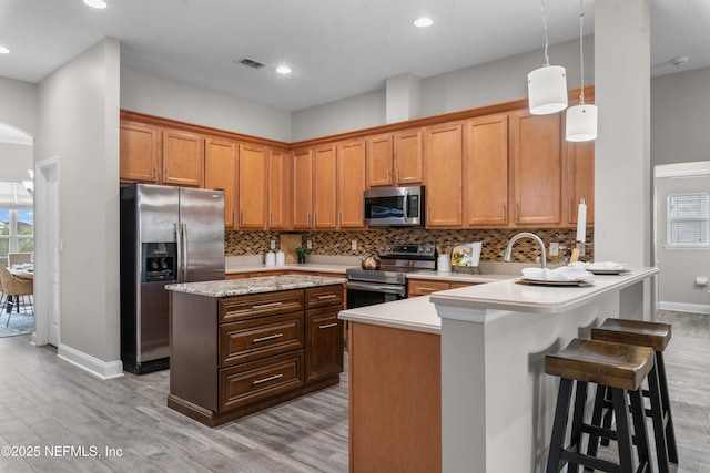 kitchen featuring decorative light fixtures, tasteful backsplash, a kitchen bar, kitchen peninsula, and stainless steel appliances