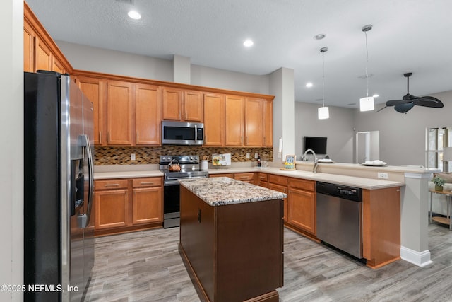 kitchen with pendant lighting, appliances with stainless steel finishes, a center island, tasteful backsplash, and kitchen peninsula