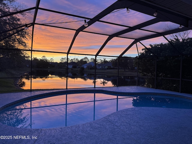 pool at dusk featuring a water view and a lanai