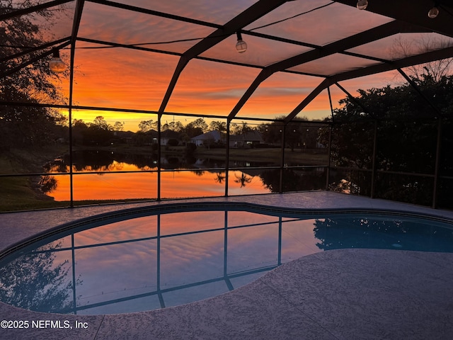 pool at dusk with a patio, glass enclosure, and a water view