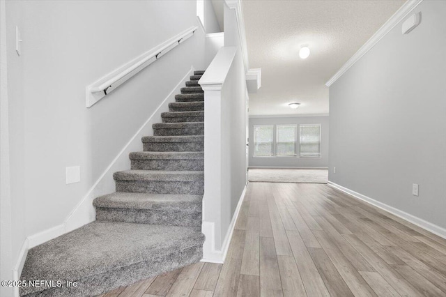 stairway with a textured ceiling, ornamental molding, and hardwood / wood-style floors