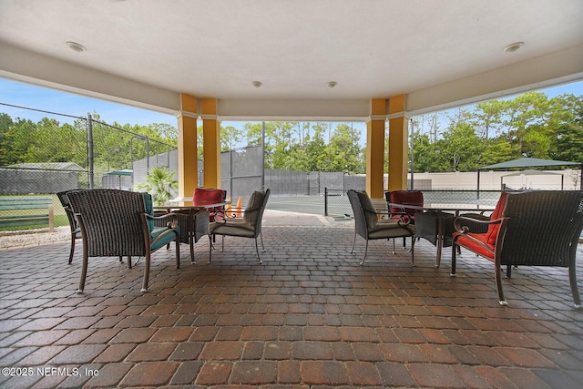 view of patio / terrace with a tennis court, outdoor dining area, and fence