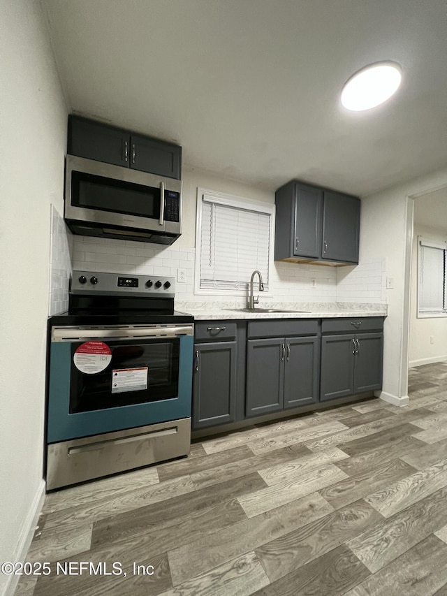 kitchen featuring decorative backsplash, sink, light wood-type flooring, stainless steel appliances, and gray cabinets