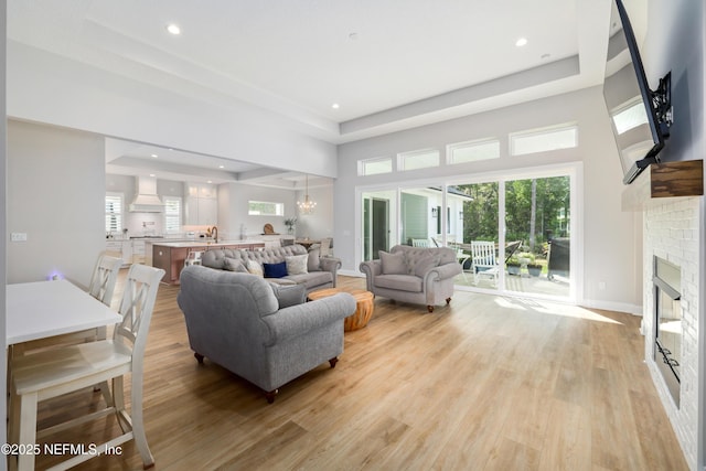 living room with a brick fireplace, a chandelier, light hardwood / wood-style floors, and a tray ceiling