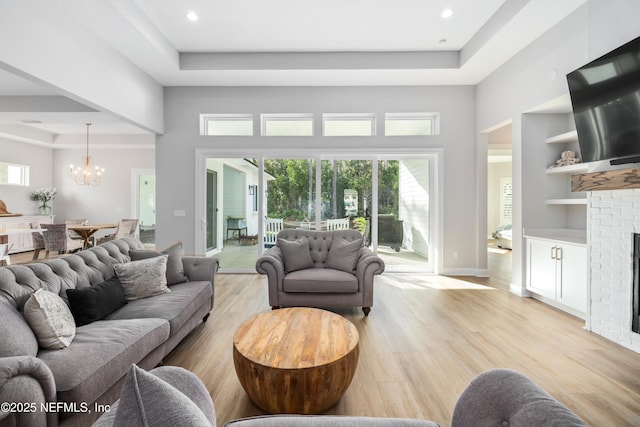 living room with an inviting chandelier, a raised ceiling, built in shelves, and light hardwood / wood-style flooring