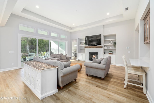 living room featuring a raised ceiling, light hardwood / wood-style floors, and built in features