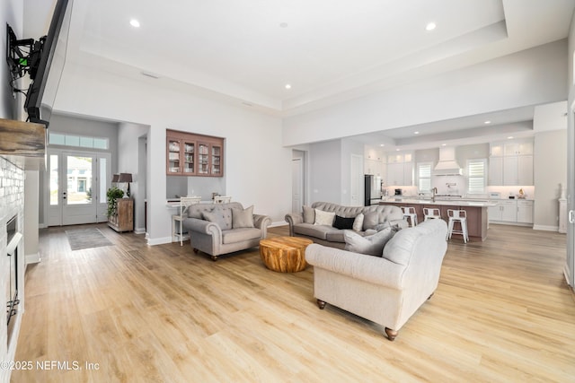 living room with a brick fireplace, sink, a raised ceiling, and light wood-type flooring