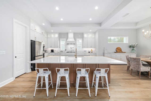 kitchen featuring custom exhaust hood, white cabinetry, a large island, and light hardwood / wood-style flooring