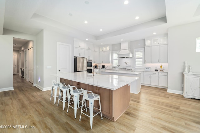 kitchen with stainless steel appliances, light wood-type flooring, white cabinets, and a large island with sink