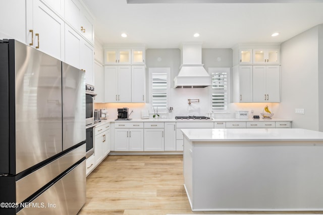 kitchen featuring stainless steel appliances, a kitchen island, custom range hood, and white cabinets