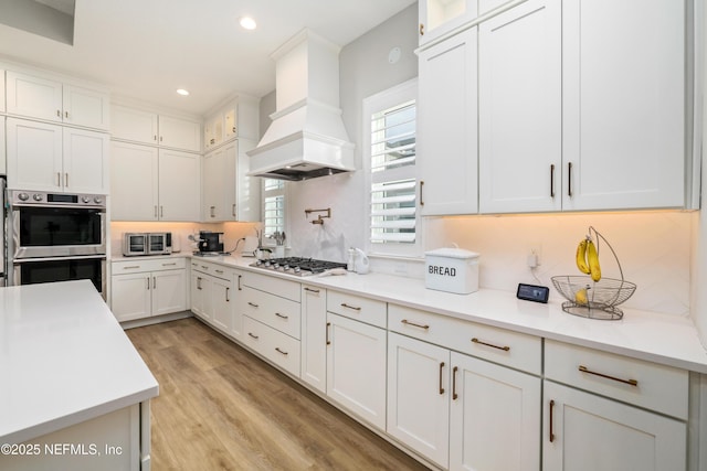 kitchen with light hardwood / wood-style flooring, appliances with stainless steel finishes, white cabinets, and premium range hood