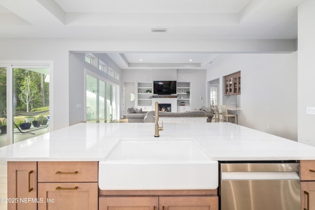 kitchen with sink, built in features, dishwasher, a tray ceiling, and light brown cabinetry