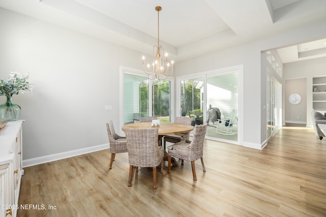 dining area with a raised ceiling, a chandelier, and light hardwood / wood-style flooring