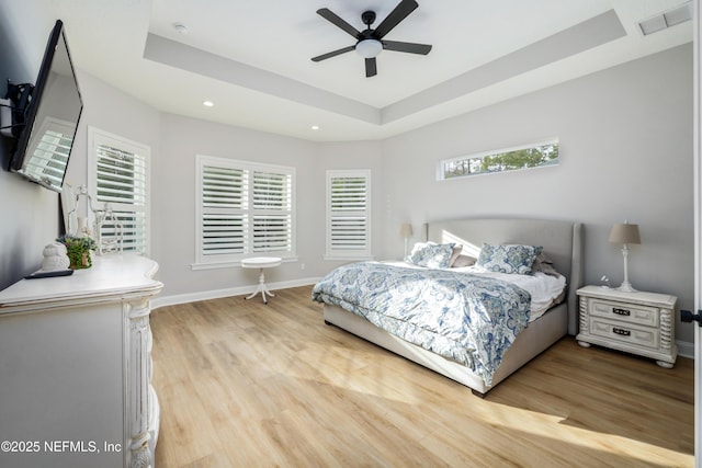 bedroom with a tray ceiling, light hardwood / wood-style flooring, and ceiling fan