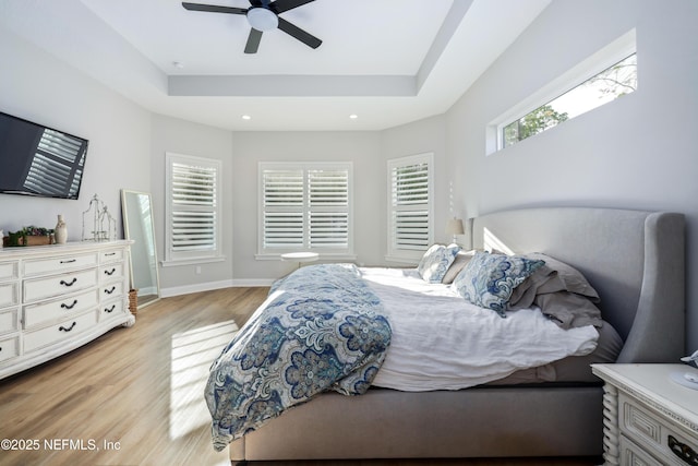 bedroom featuring multiple windows, a tray ceiling, ceiling fan, and light wood-type flooring