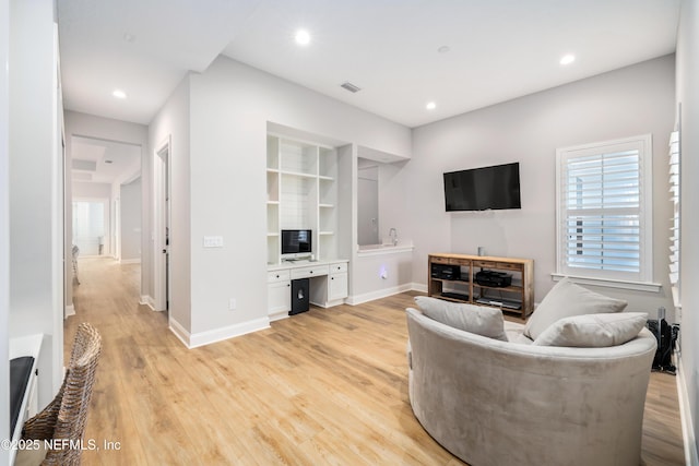 living room featuring built in features, built in desk, and light hardwood / wood-style flooring