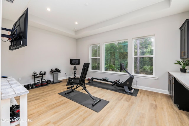 exercise area featuring a tray ceiling and light hardwood / wood-style flooring