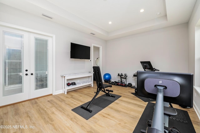 exercise area with french doors, a tray ceiling, and light hardwood / wood-style floors