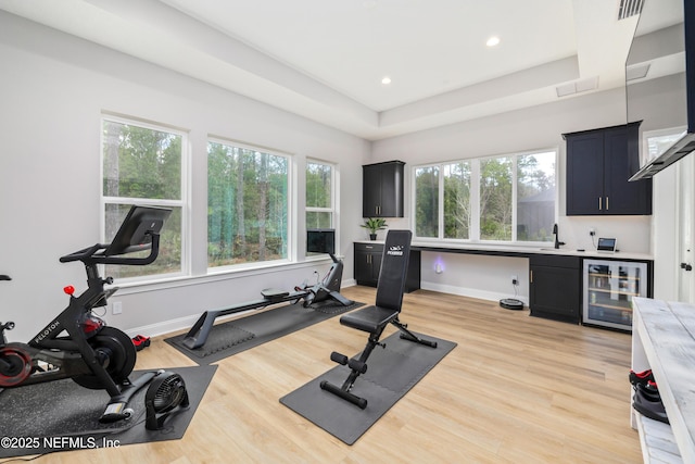 exercise area featuring beverage cooler, a raised ceiling, sink, and light hardwood / wood-style flooring