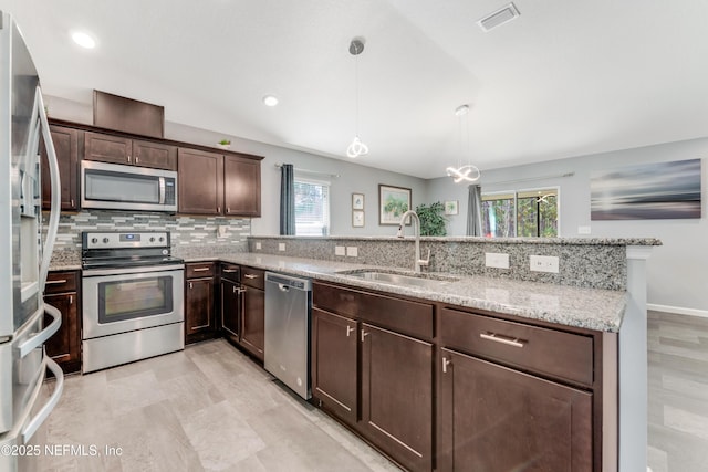 kitchen featuring sink, hanging light fixtures, light stone counters, stainless steel appliances, and dark brown cabinets